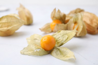 Photo of Ripe physalis fruits with calyxes on white marble table, closeup