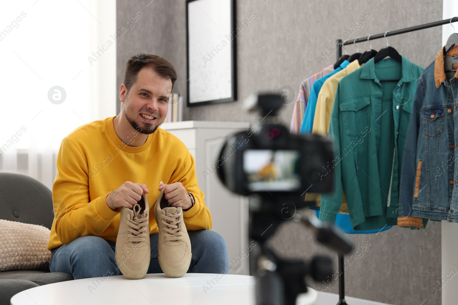 Photo of Smiling fashion blogger showing shoes while recording video at home