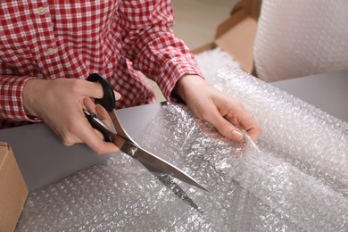 Photo of Woman cutting bubble wrap at table in warehouse, closeup