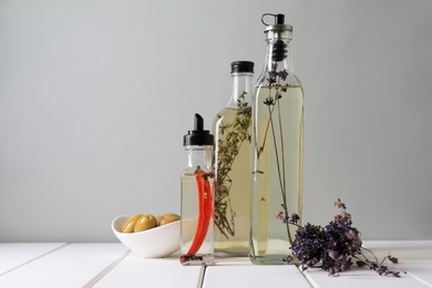 Bottles of different cooking oils, lavender flowers and olives on white wooden table against grey background