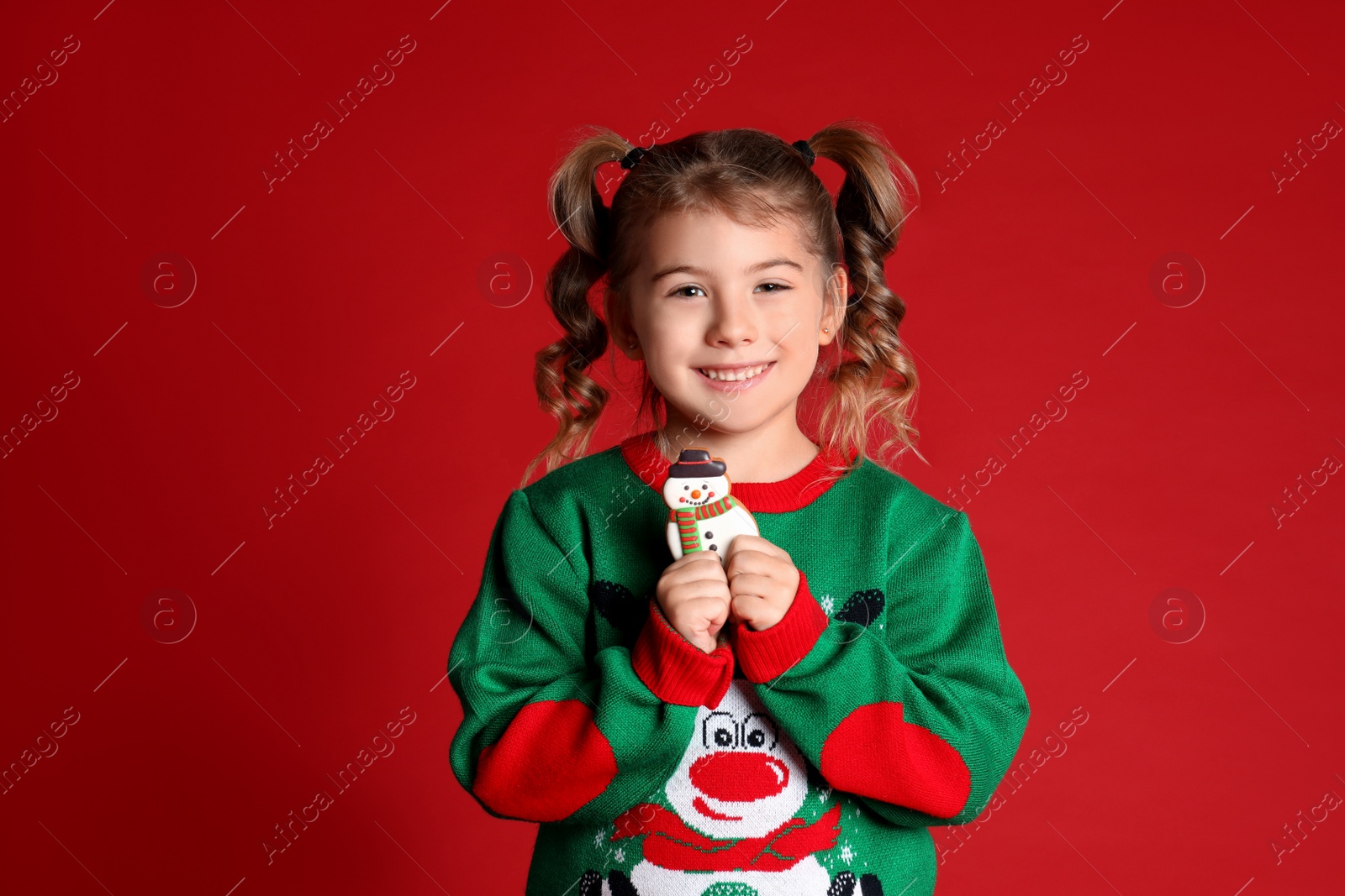 Photo of Cute little girl with Christmas gingerbread cookie on red background