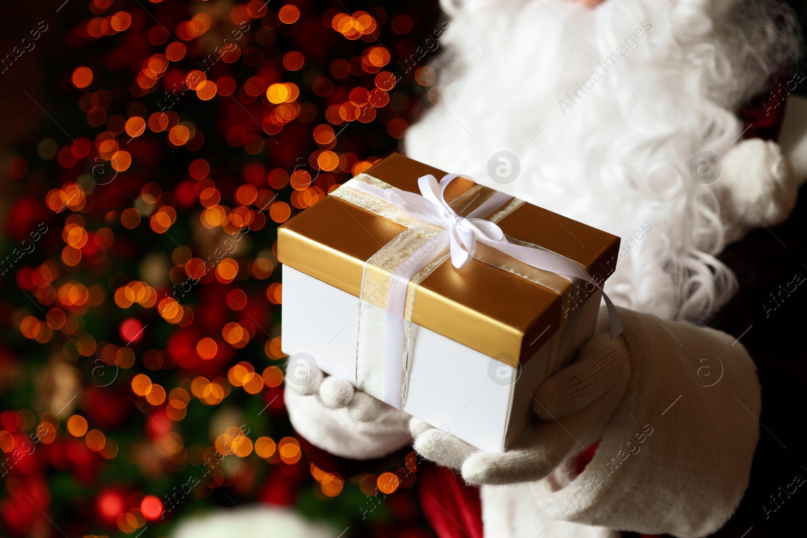 Photo of Santa Claus holding Christmas gift against blurred festive lights, closeup