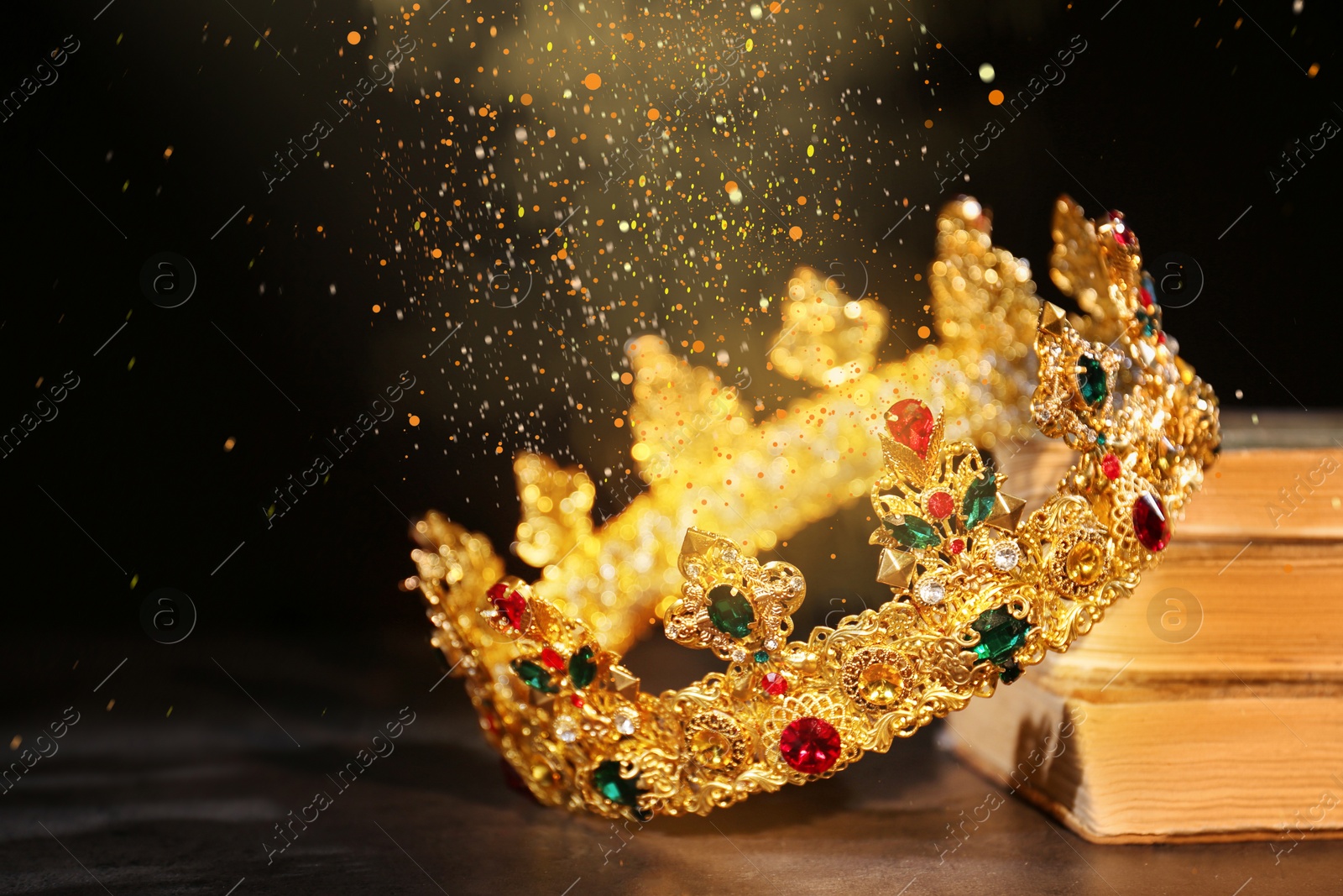 Image of Fantasy world. Beautiful golden crown and old books lit by magic light on table