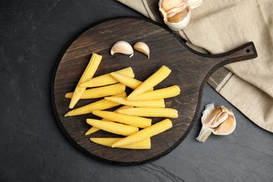Photo of Fresh baby corn cobs served on black table, flat lay