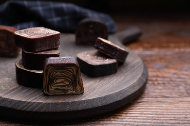 Photo of Tasty chocolate candies on wooden board. Space for text