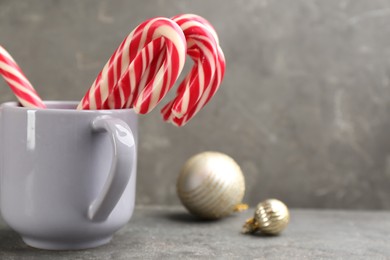 Photo of Many sweet candy canes in cup on grey table, space for text. Traditional Christmas treat