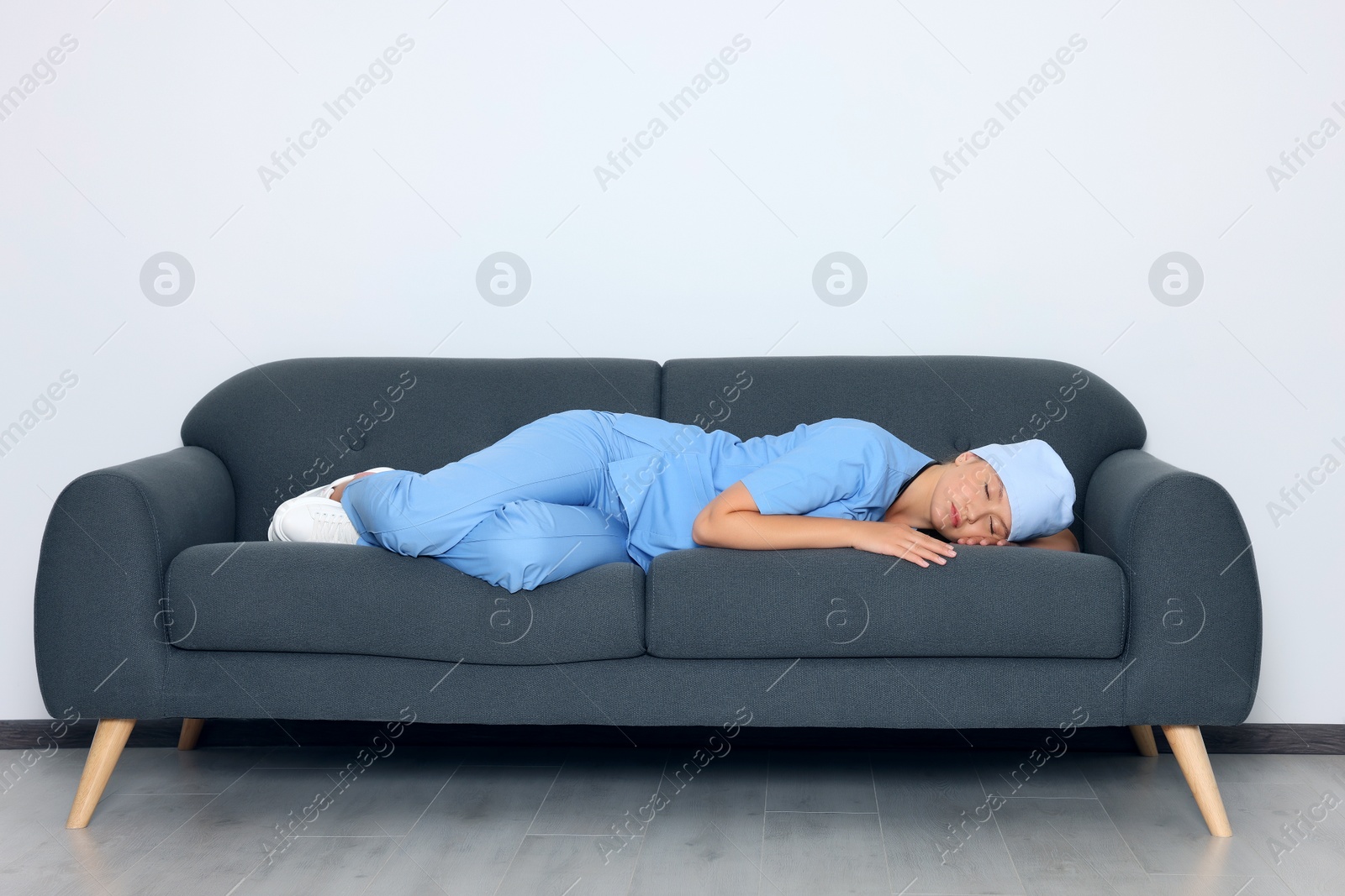 Photo of Tired young doctor sleeping on sofa indoors