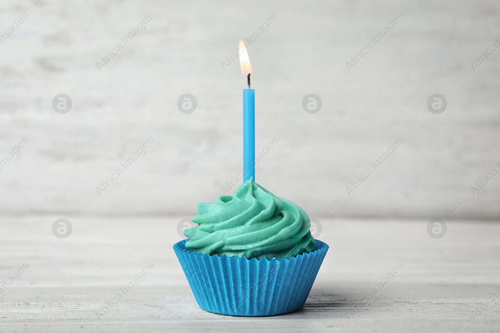 Photo of Delicious birthday cupcake with cream and burning candle on white wooden table