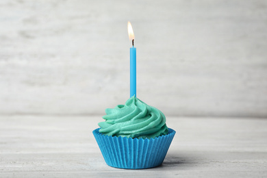 Delicious birthday cupcake with cream and burning candle on white wooden table