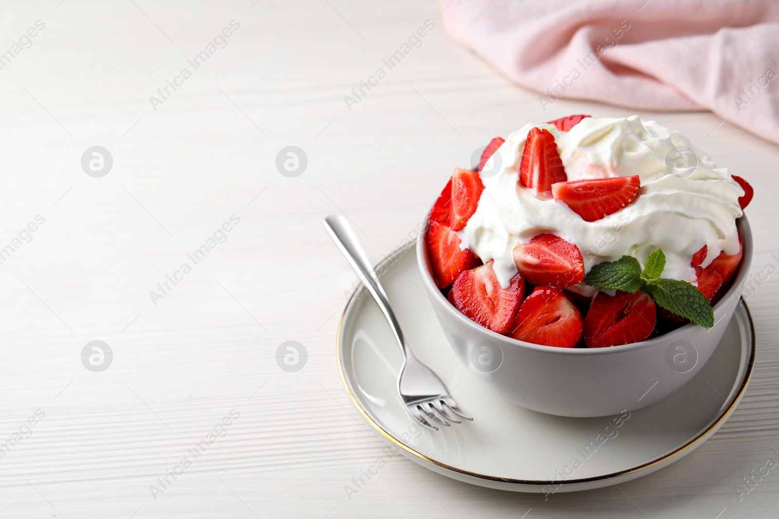 Photo of Delicious strawberries with whipped cream served on white wooden table. Space for text