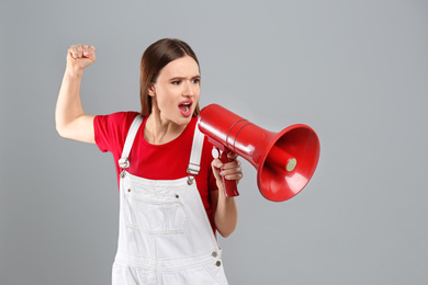 Photo of Emotional young woman with megaphone on light grey background