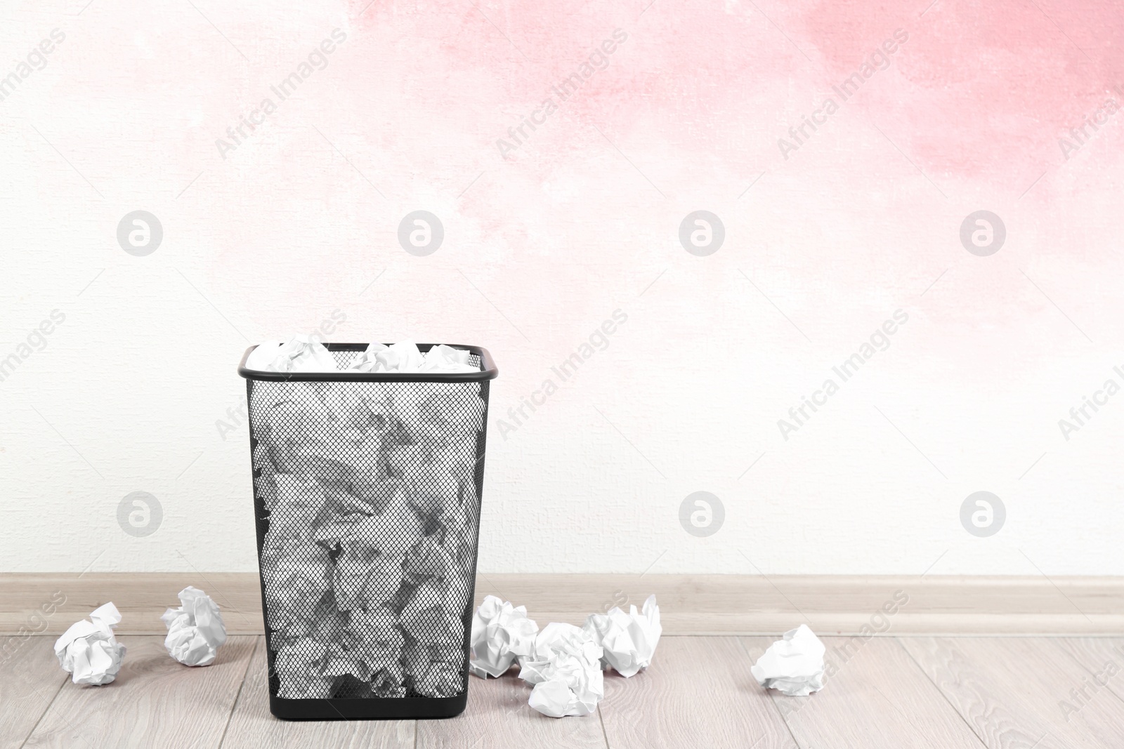 Photo of Basket with crumpled paper balls near pink wall. Space for text