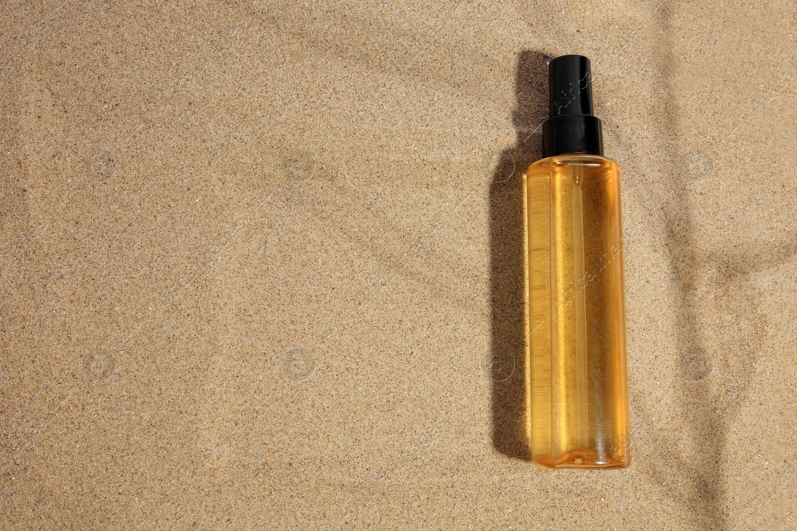 Photo of Bottle with serum on sand, top view and space for text. Cosmetic product