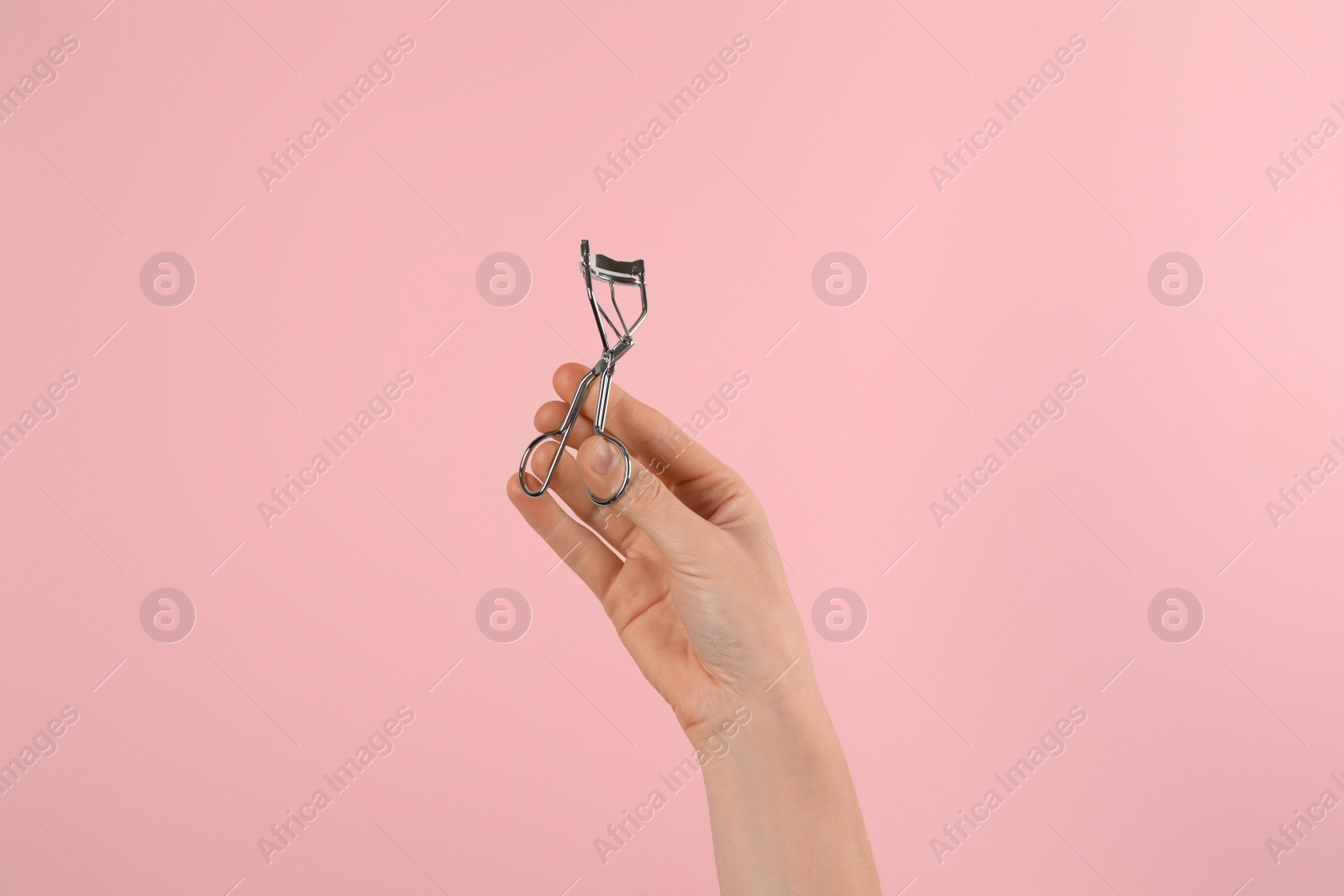 Photo of Woman holding eyelash curler on pink background, closeup. Makeup tool