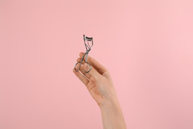 Woman holding eyelash curler on pink background, closeup. Makeup tool