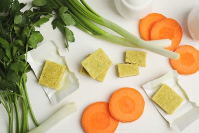 Photo of Bouillon cubes and other ingredients for soup on white wooden table, flat lay