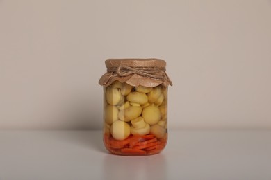 Photo of Jar of tasty pickled mushrooms on white table