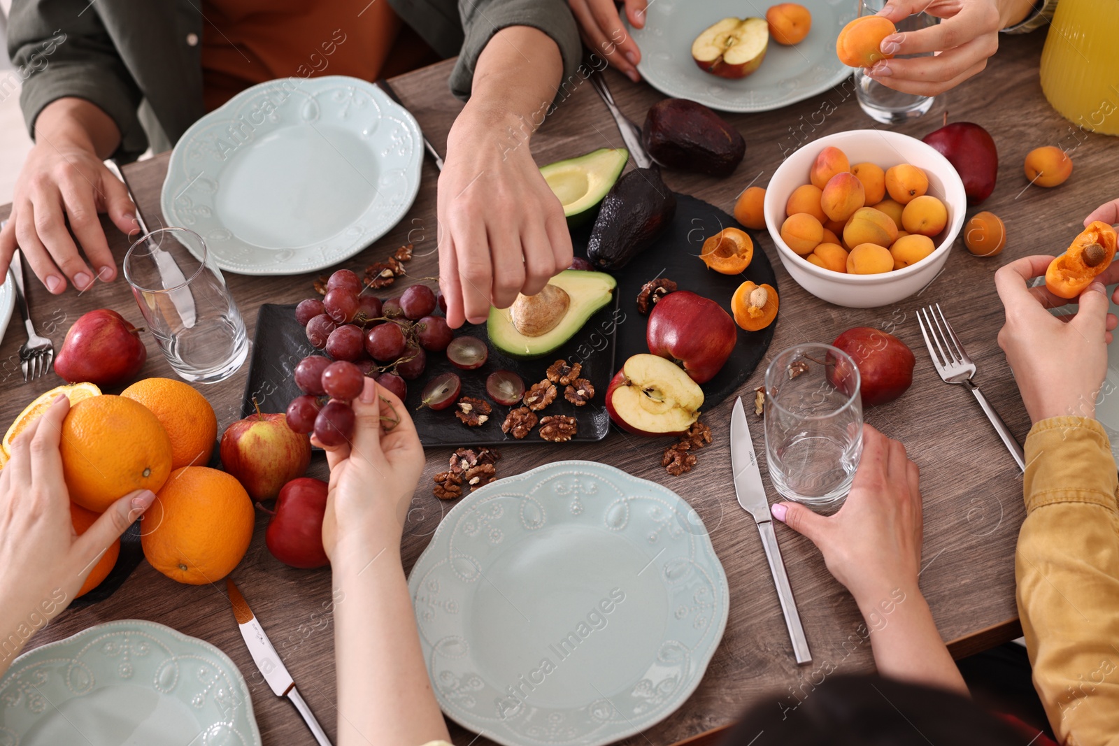 Photo of Friends eating vegetarian food at wooden table indoors, closeup