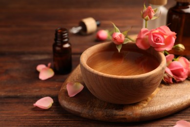 Photo of Bowl of essential oil and beautiful roses on wooden table. Aromatherapy treatment