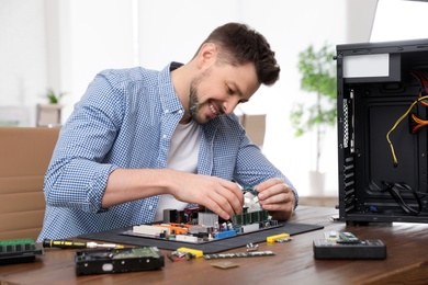 Photo of Male technician repairing motherboard at table indoors