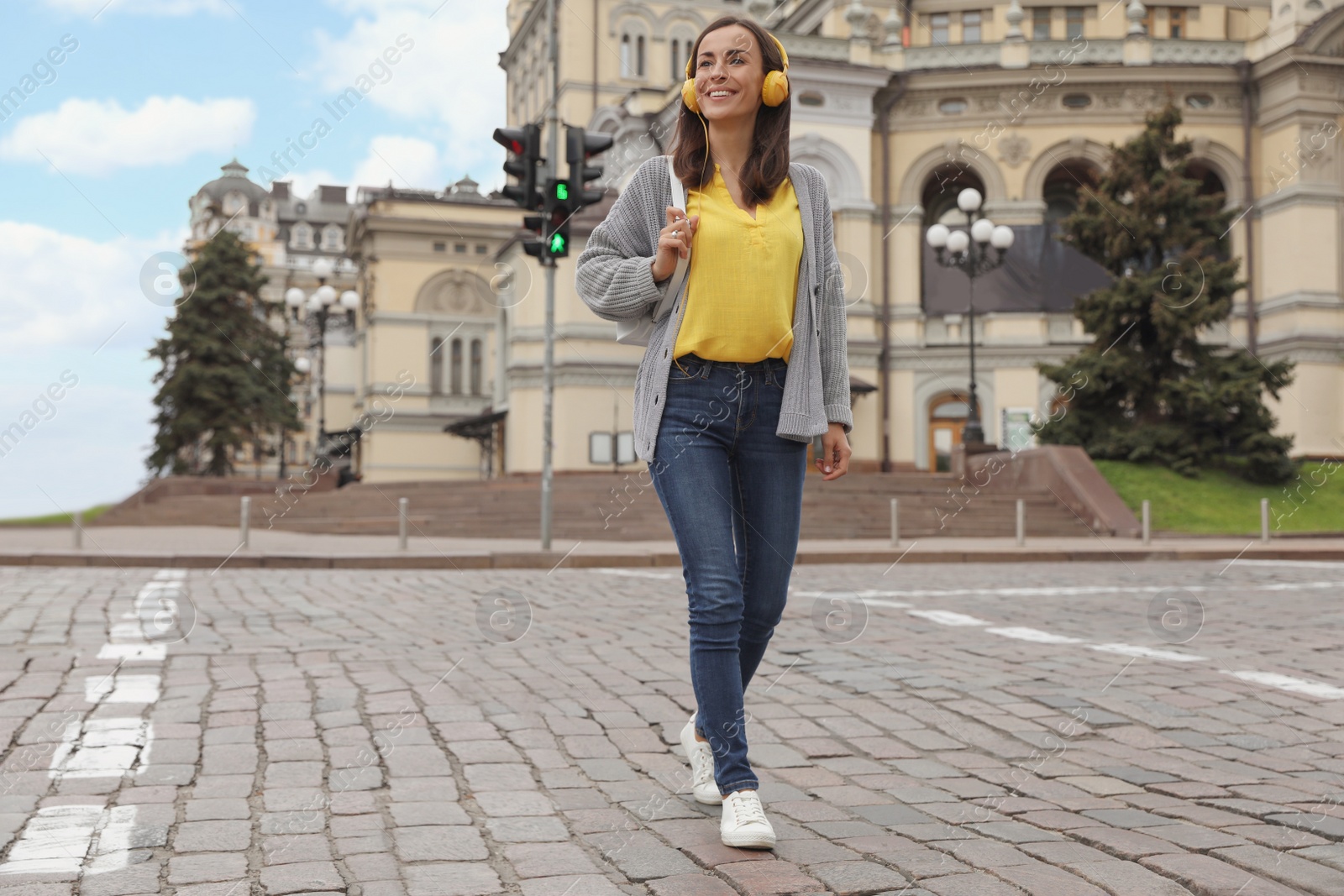 Photo of Young woman with headphones crossing street. Traffic rules and regulations