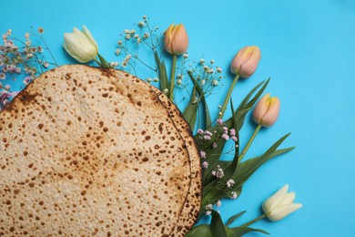 Photo of Tasty matzos and fresh flowers on light blue background, flat lay. Passover (Pesach) celebration