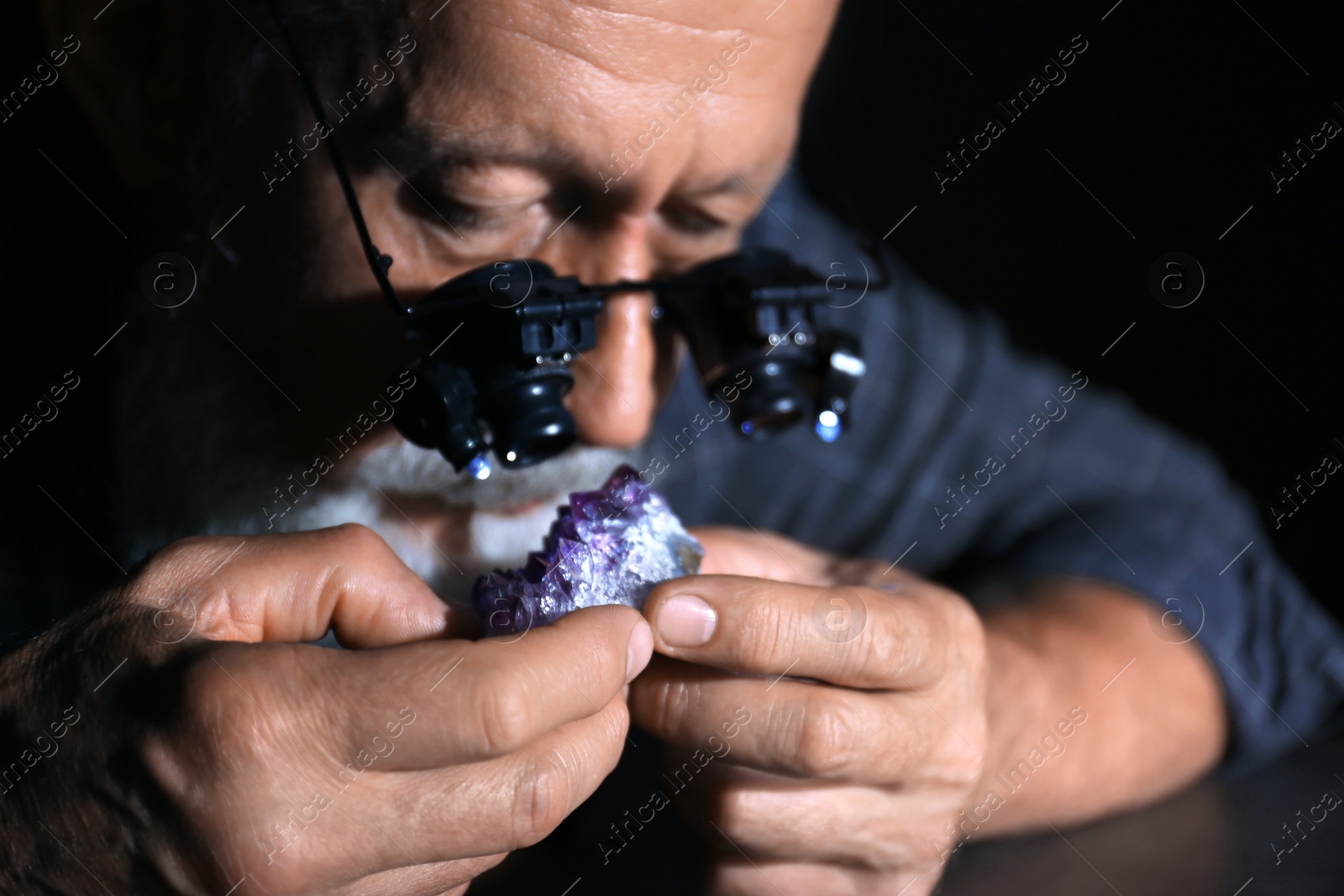 Photo of Male jeweler evaluating amethyst in workshop, closeup view