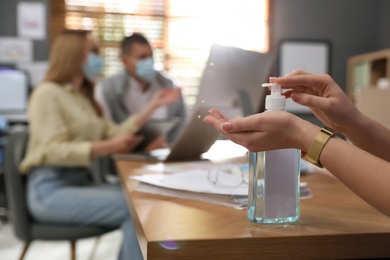 Office worker using hand sanitizer at table, closeup. Personal hygiene during COVID-19 pandemic