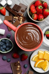 Photo of Fondue pot with melted chocolate, marshmallows, fresh orange and different berries on grey table, flat lay