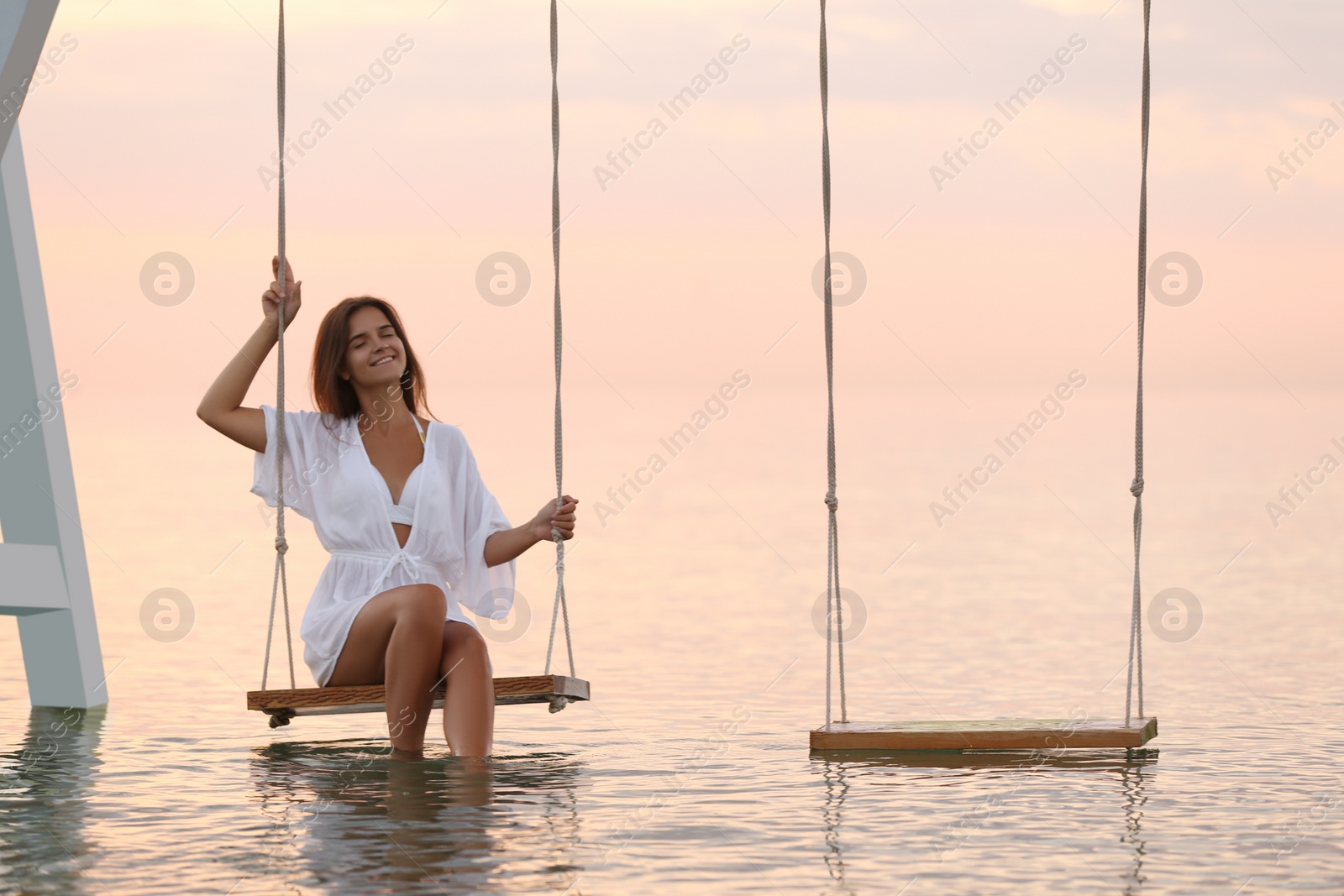 Photo of Young woman enjoying sunrise on swing over water