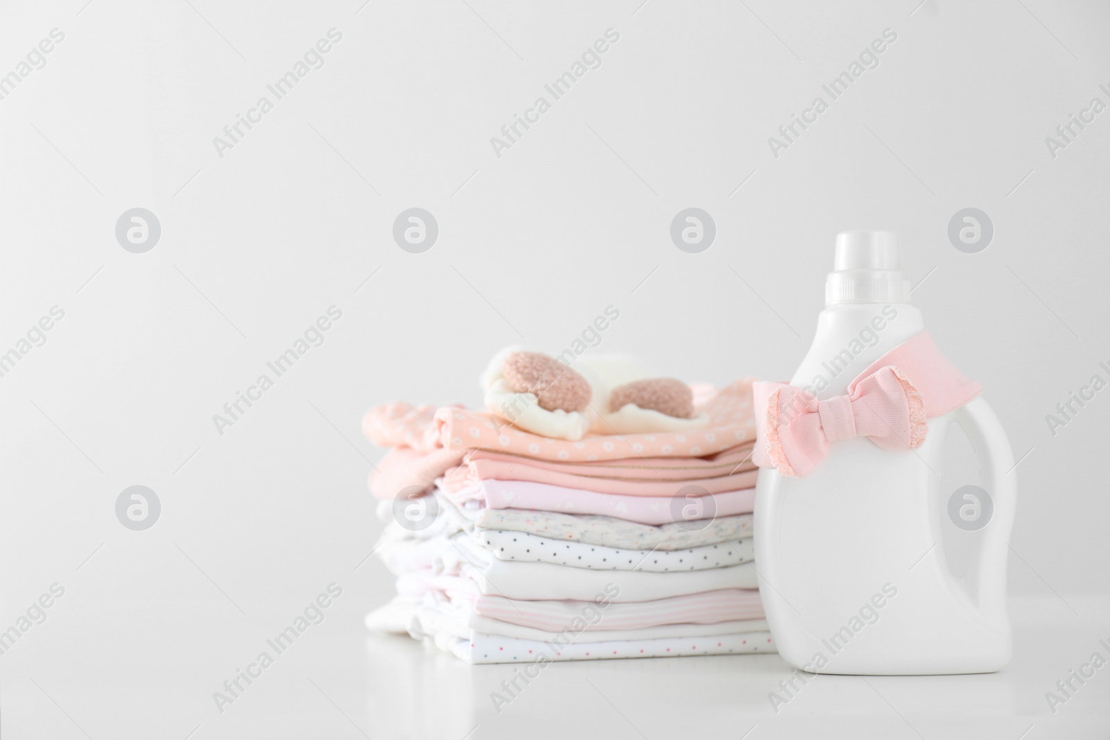 Photo of Detergent and children's clothes on white table