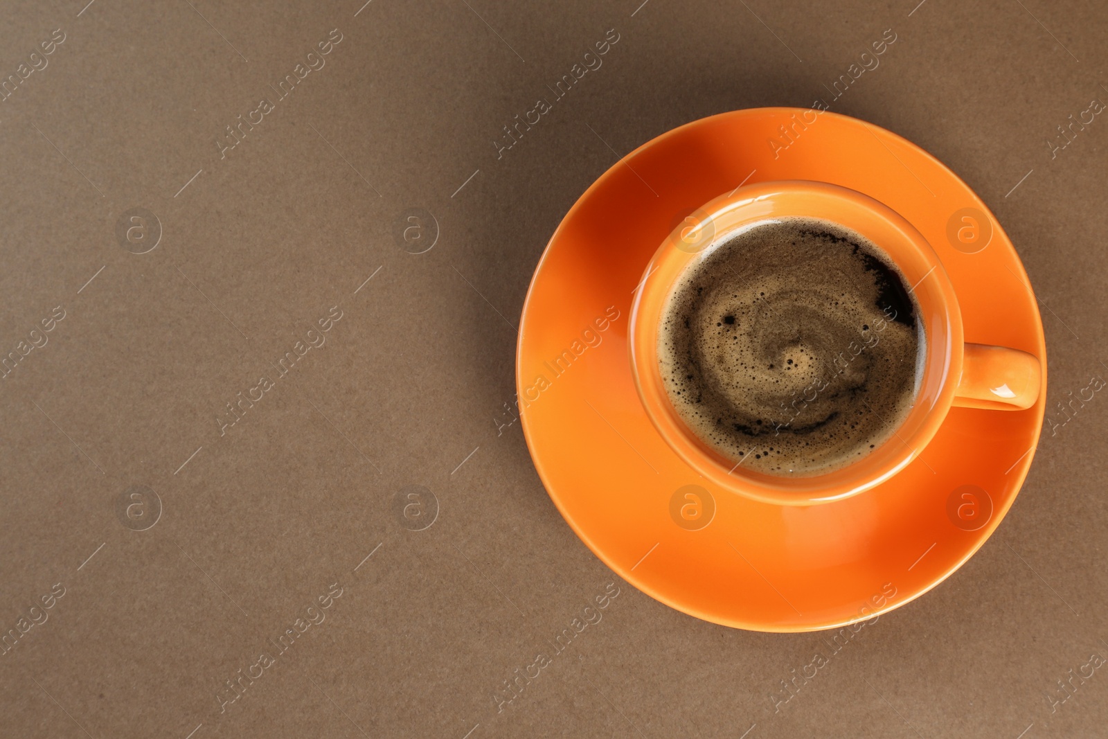 Photo of Coffee in cup on brown background, top view. Space for text