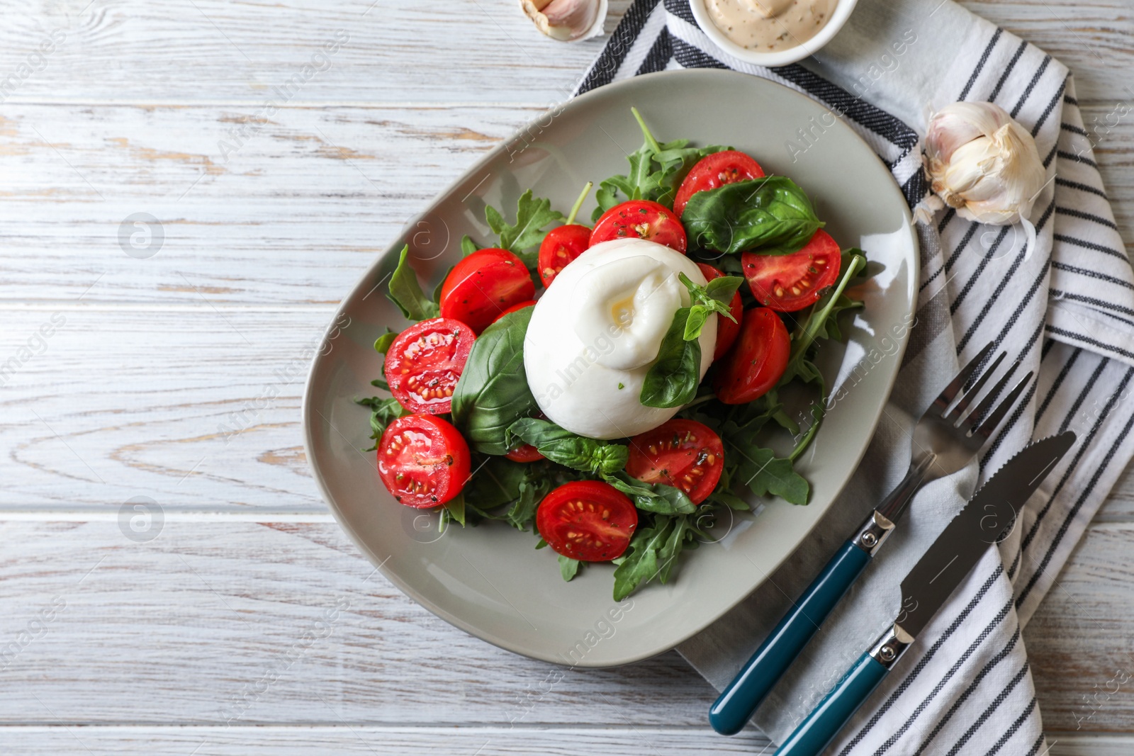 Photo of Delicious burrata cheese served with tomatoes and basil on white wooden table, flat lay. Space for text