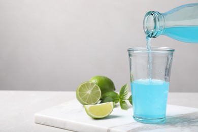 Pouring refreshing light blue drink into glass on white table, space for text