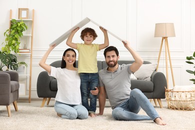 Photo of Housing concept. Happy family holding plastic roof on floor at home