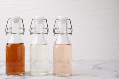 Different types of vinegar in bottles on light marble table, closeup. Space for text