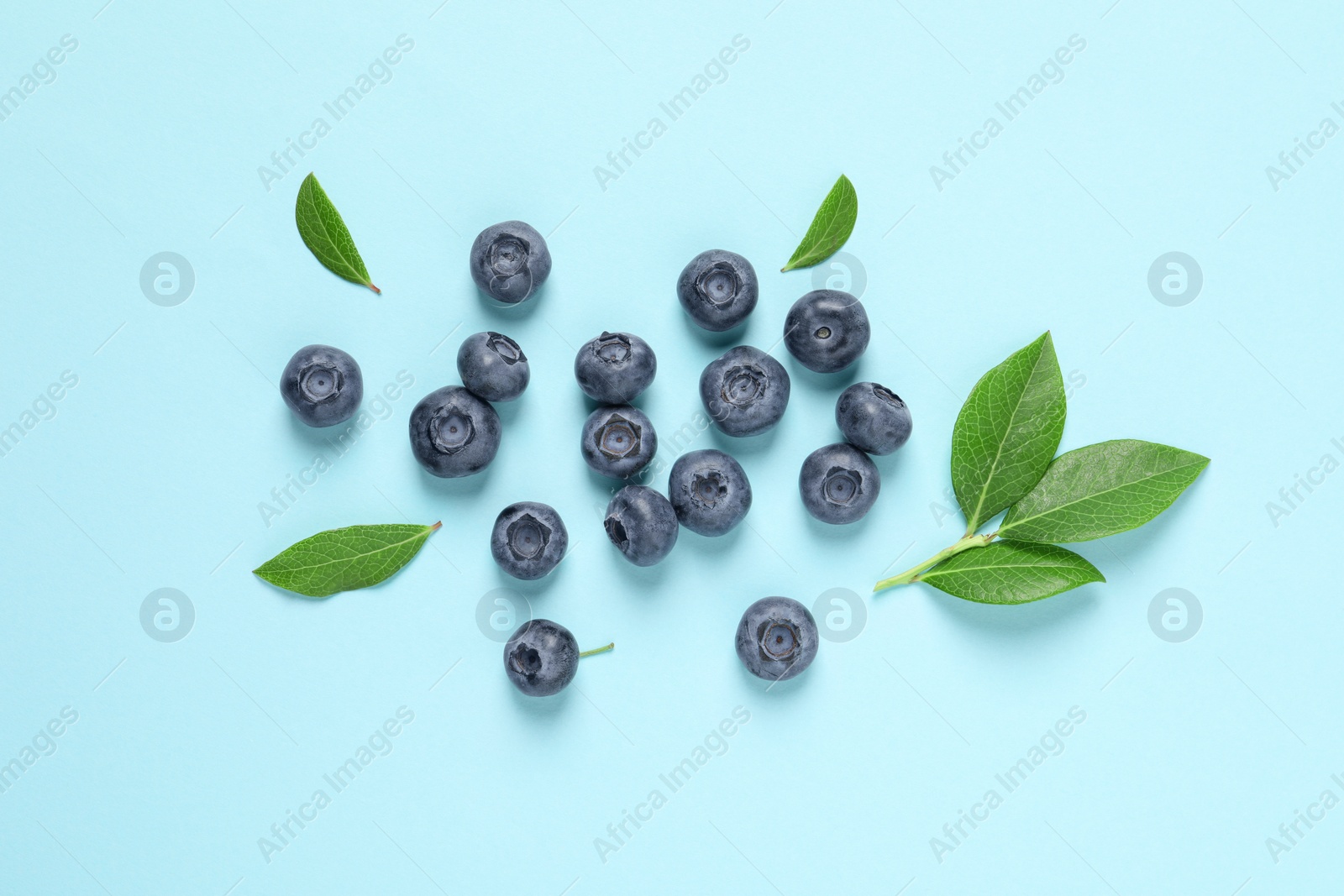 Photo of Tasty fresh blueberries with green leaves on light blue background, flat lay