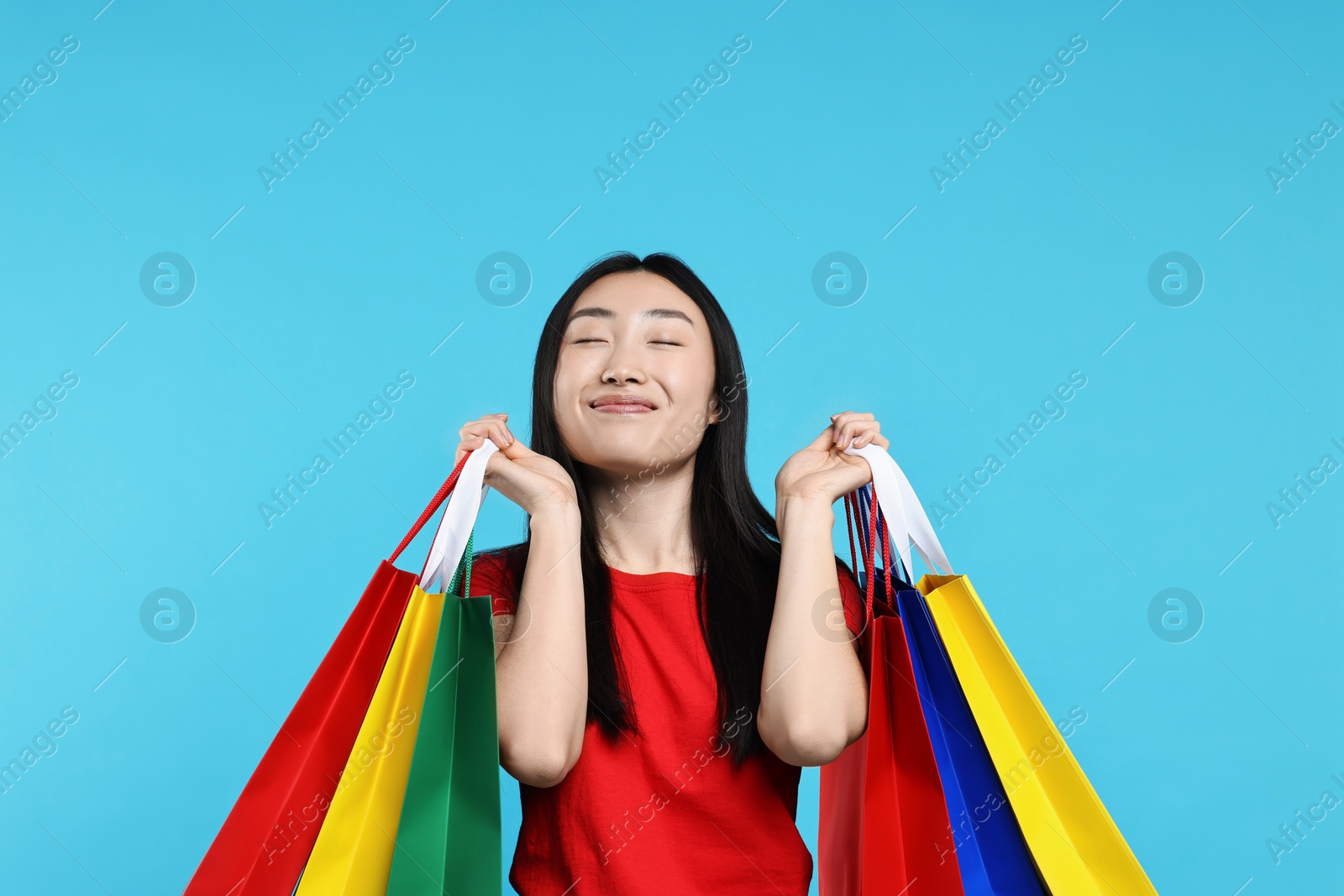 Photo of Happy woman with shopping bags on light blue background