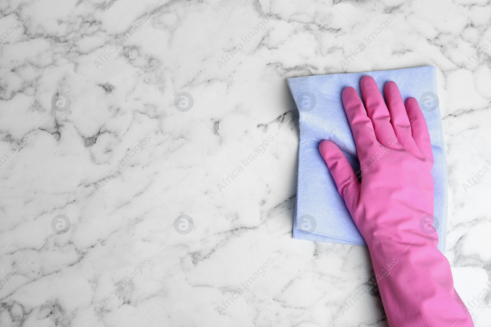 Photo of Woman in gloves wiping white marble table with rag, top view. Space for text