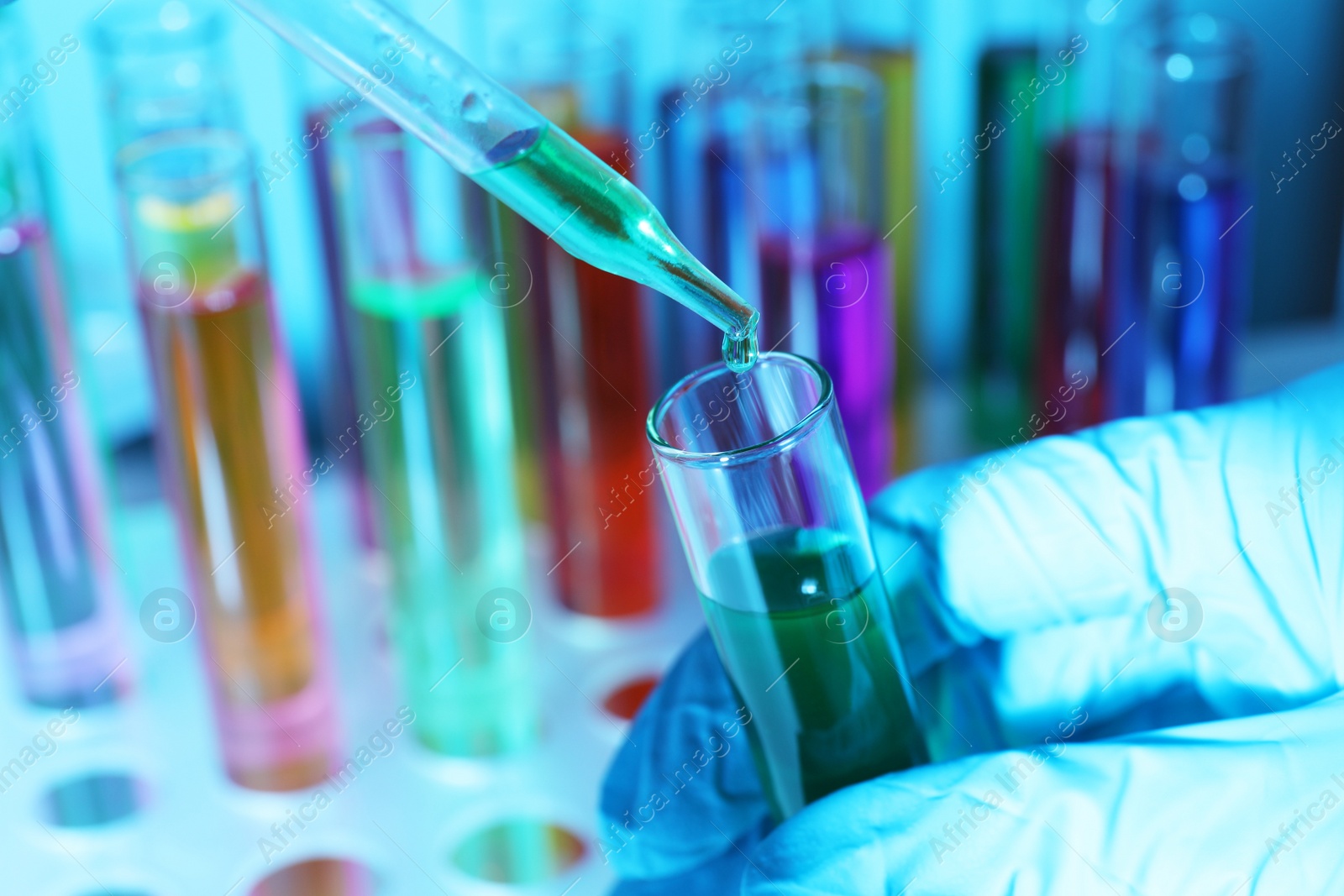 Photo of Scientist dripping liquid from pipette into test tube against laboratory glassware, closeup