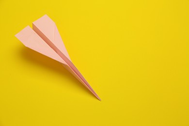 Handmade light pink paper plane on yellow background, above view. Space for text