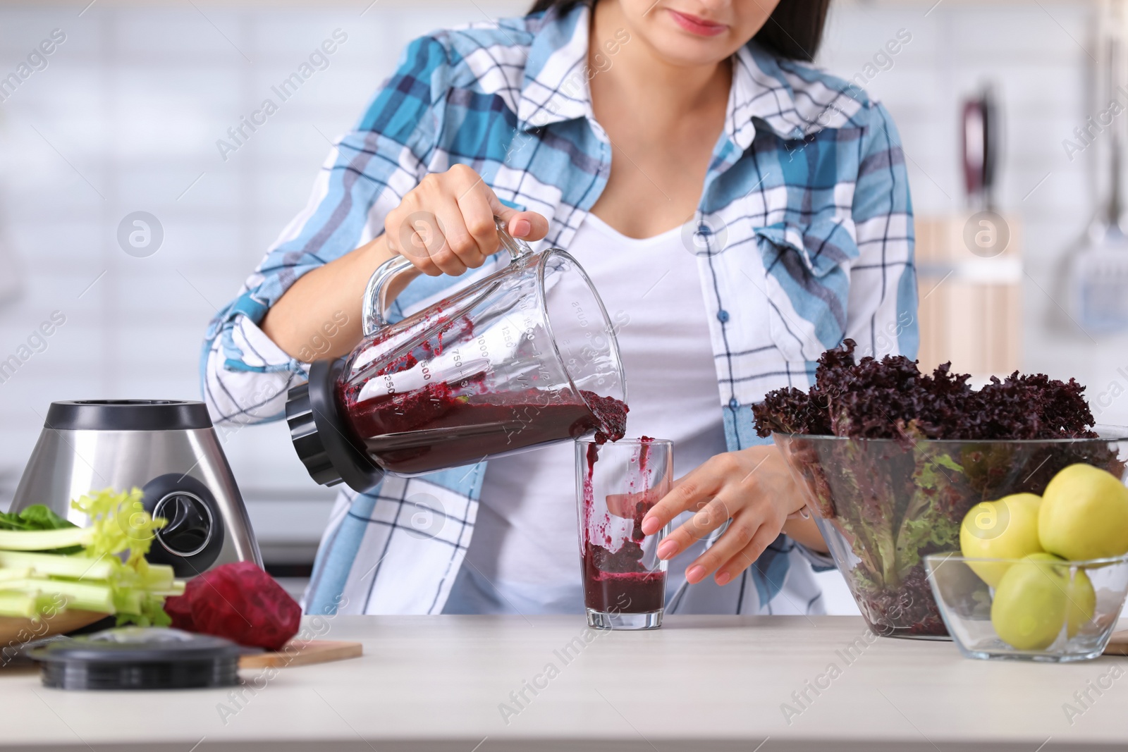 Photo of Young woman pouring tasty healthy smoothie into glass at table in kitchen