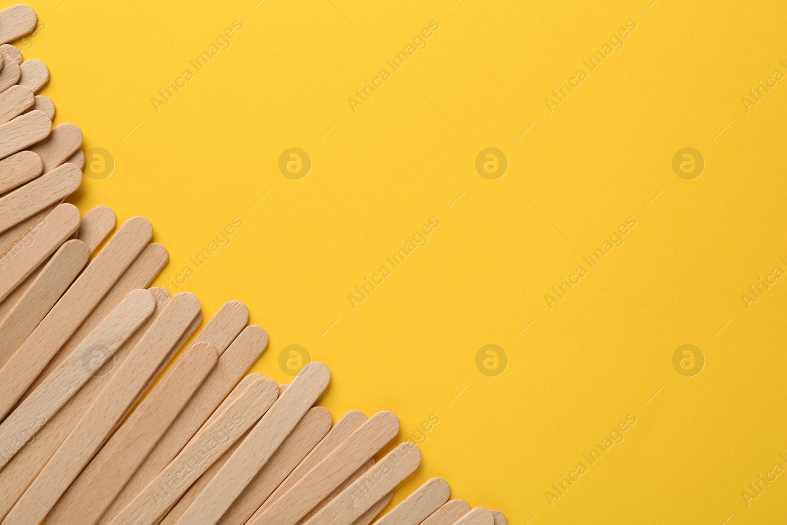 Photo of Wooden waxing spatulas on yellow background, flat lay. Space for text