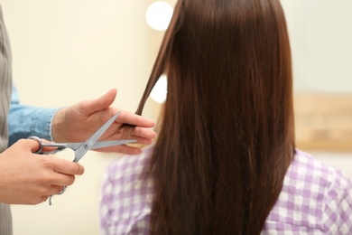 Photo of Barber making stylish haircut with professional scissors in beauty salon, closeup