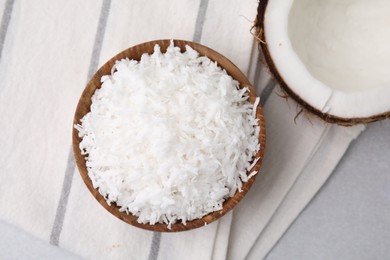 Coconut flakes in bowl and nut on light grey table, top view