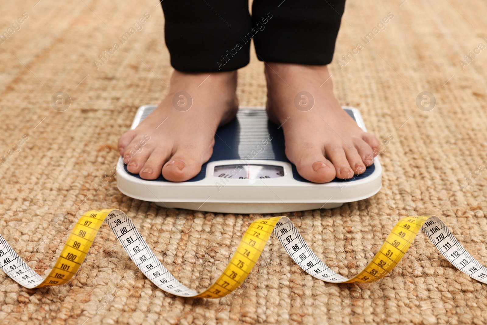 Photo of Woman using scales on carpet near measuring tape, closeup. Overweight problem