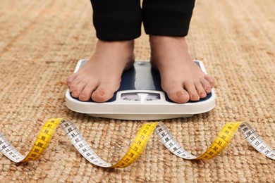 Woman using scales on carpet near measuring tape, closeup. Overweight problem