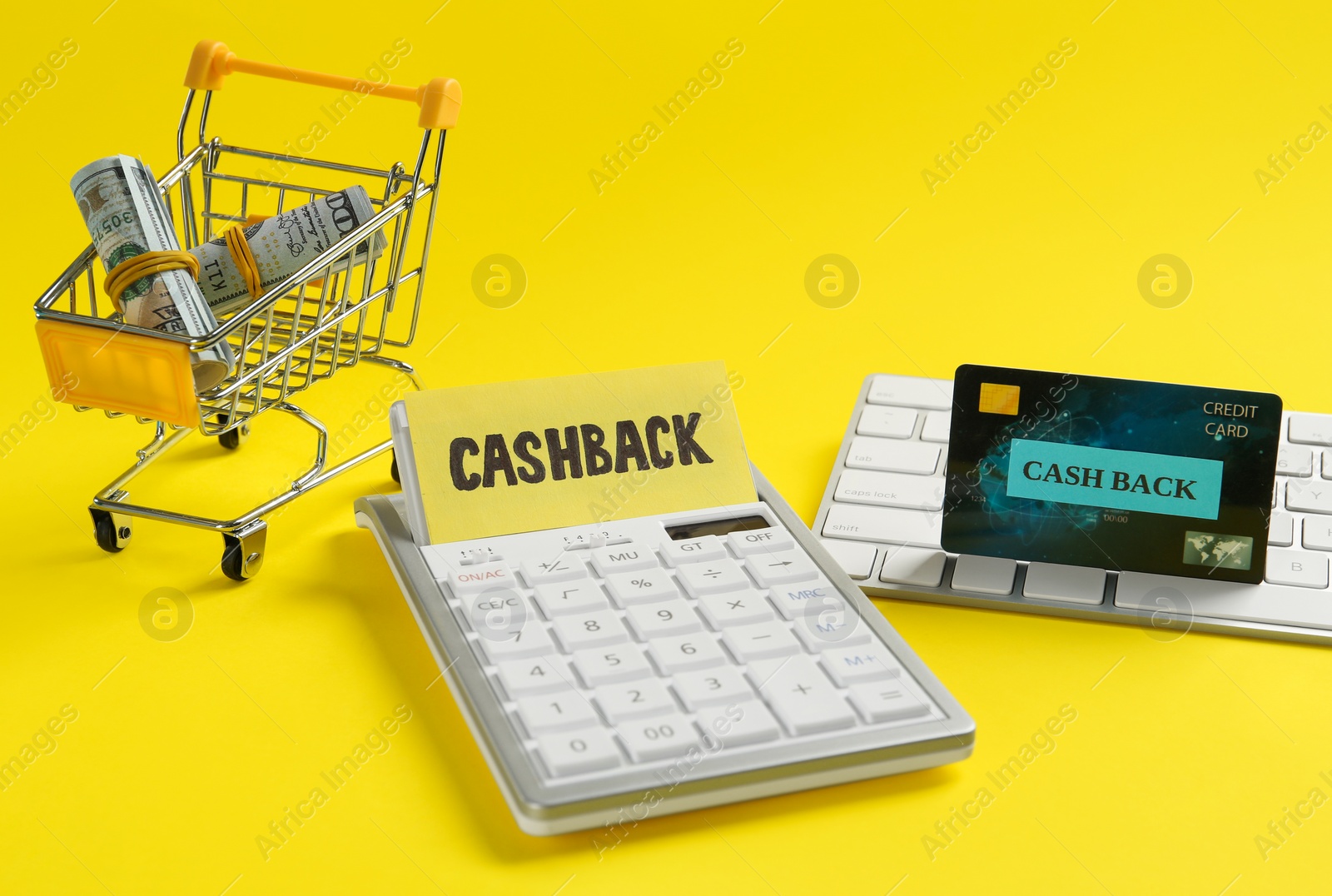 Photo of Calculator, keyboard, credit card and dollar banknotes in shopping cart on yellow background. Cashback concept