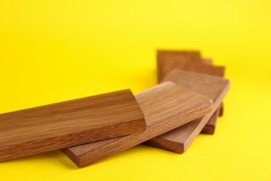 Photo of Falling wooden domino tiles on yellow background, closeup