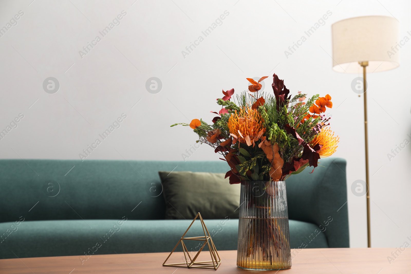 Photo of Vase with bouquet of beautiful flowers on wooden table near sofa in living room, space for text